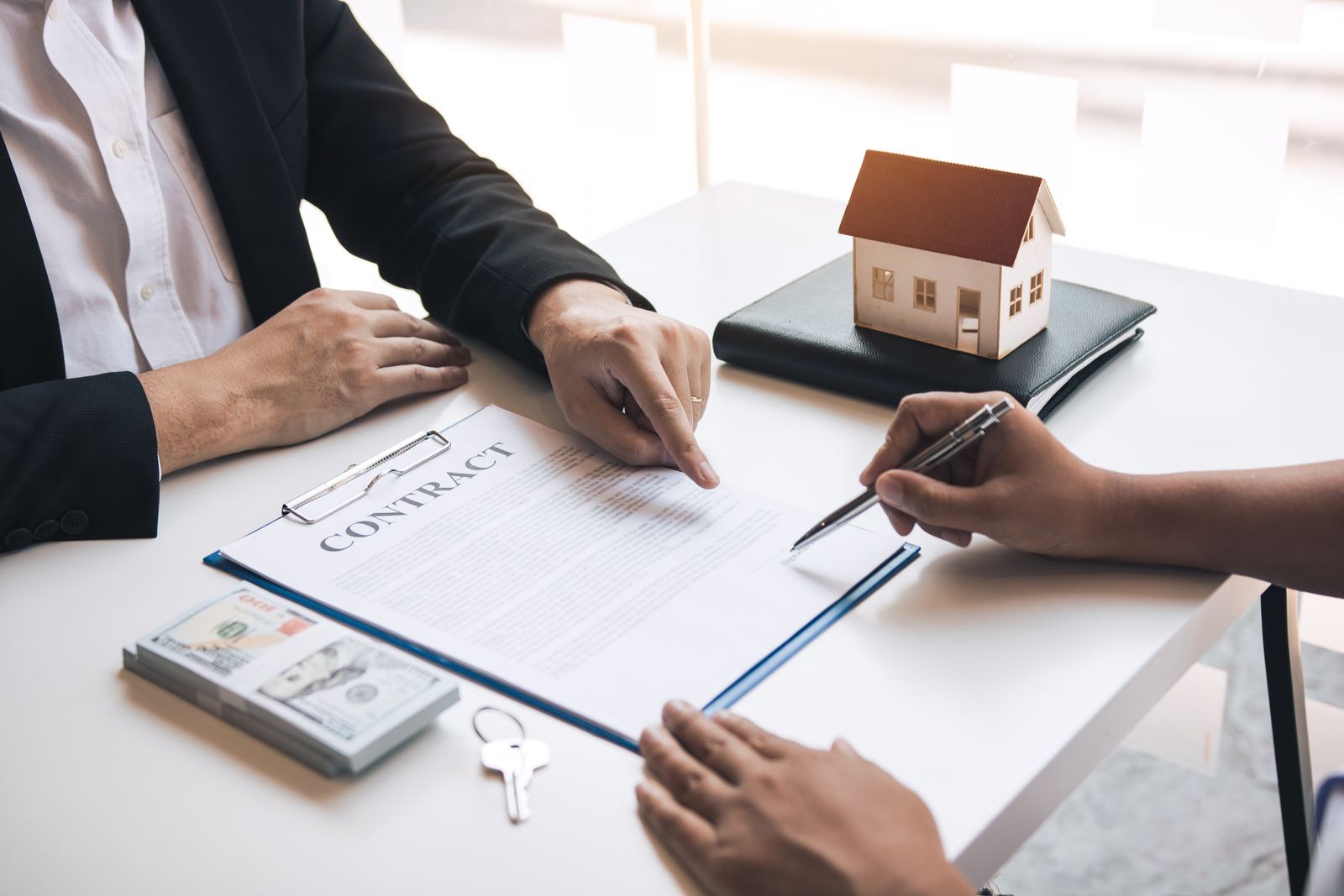 Real estate paperwork being signed beside a model house